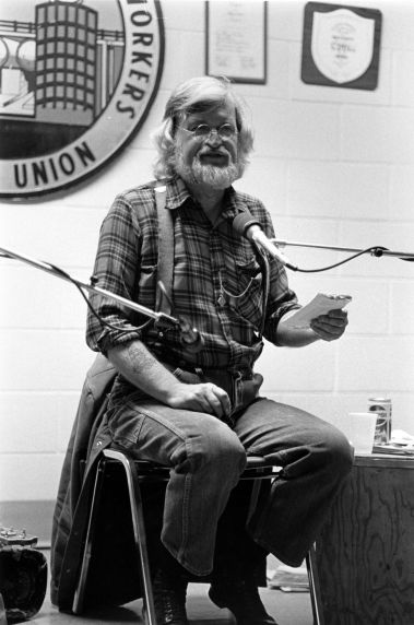 (32373) Utah Phillips Holding a Booklet and Speaking During a Performance, circa 1980